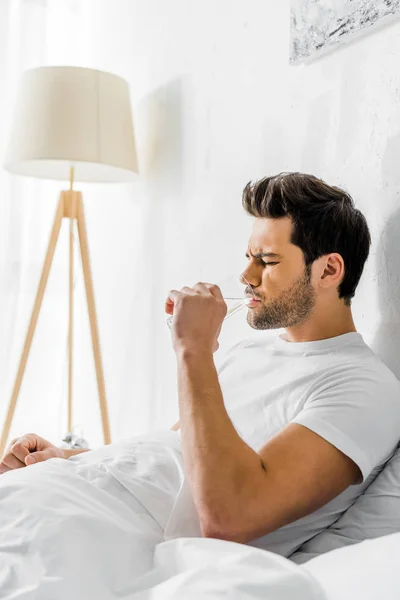 Müder Mann mit Kopfschmerzen trinkt morgens Wasser im Bett — Stockfoto