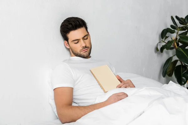 Красивый молодой человек спит в постели с книгой — стоковое фото