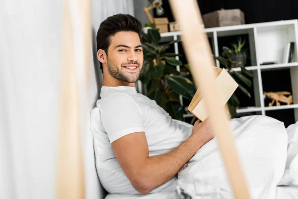 Happy young man with book in bed in the morning — Stock Photo