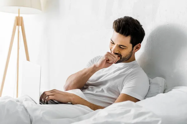 Красивый смеющийся человек, использующий ноутбук в постели по утрам — стоковое фото