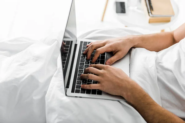 Частковий вид людини, що використовує ноутбук у ліжку — стокове фото