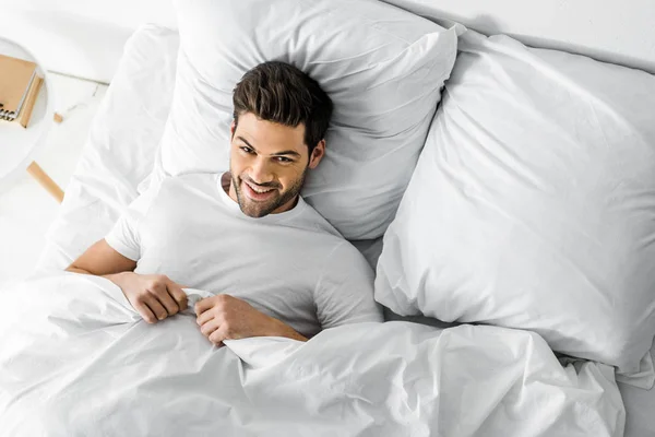 Vue de dessus de bel homme joyeux couché dans le lit le matin — Photo de stock