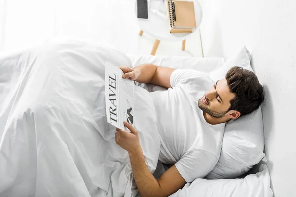 Schöner Mann liest Reisezeitung im Bett — Stockfoto