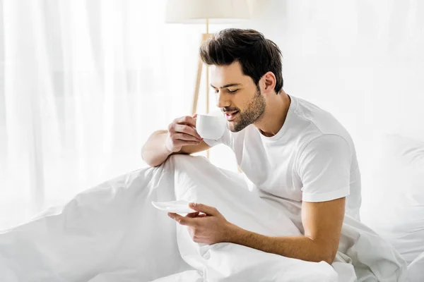 Усміхнений чоловік в піжамі, пити каву в ліжку з ранку — стокове фото