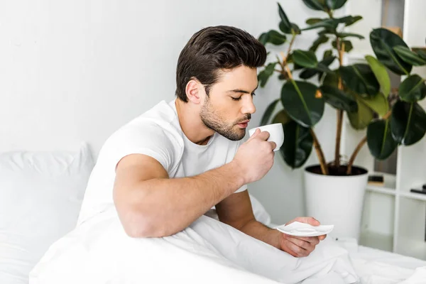 Schöner Mann im Schlafanzug, der morgens im Bett Kaffee trinkt — Stockfoto