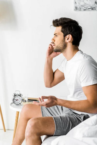 Worried man talking on smartphone while sitting on bed in the morning — Stock Photo