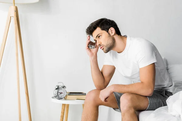 Upset man with glass of water sitting on bed in the morning — Stock Photo
