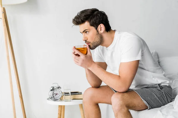 Handsome man in pajamas drinking tea in bedroom — Stock Photo