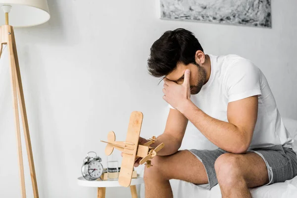 Aufgebrachter Mann hält Holzspielzeugflugzeug im Schlafzimmer — Stockfoto