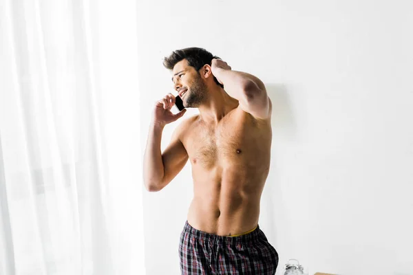 Мужчина без рубашки разговаривает по смартфону в спальне — стоковое фото