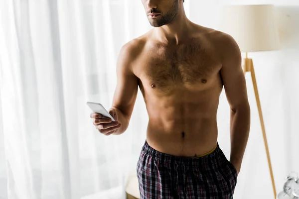 Ausgeschnittene Ansicht eines hemdslosen Mannes, der sein Smartphone zu Hause benutzt — Stockfoto