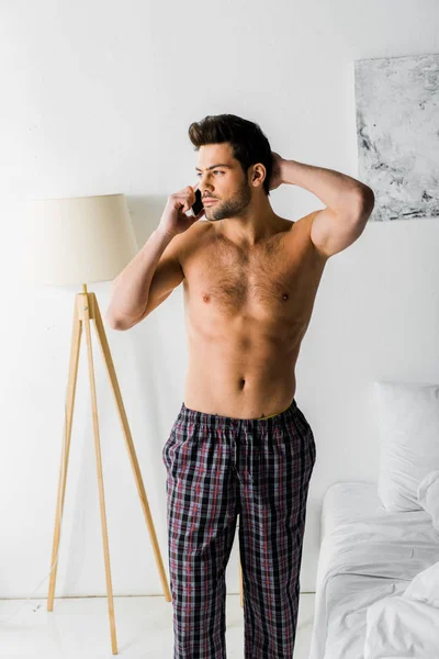 Shirtless thoughtful man talking on smartphone in bedroom — Stock Photo
