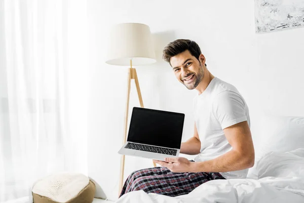 Bel homme souriant montrant ordinateur portable avec écran vierge — Photo de stock