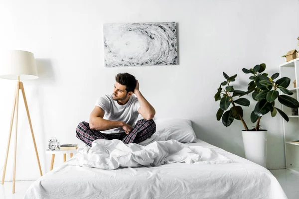 Bonito pensivo homem de pijama sentado na cama de manhã — Fotografia de Stock