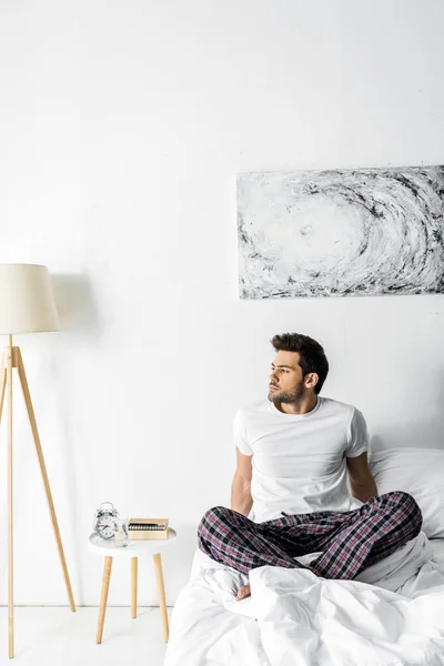 Homem pensativo de pijama sentado na cama pela manhã — Fotografia de Stock