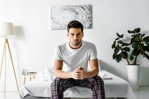 Handsome confident man in pajamas sitting on bed at home — Stock Photo