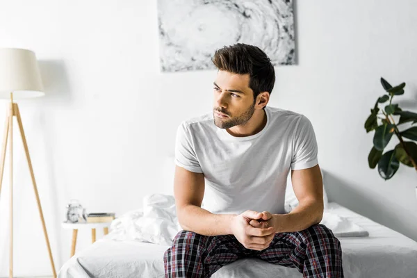 Handsome thoughtful man in pajamas sitting on bed in the morning — Stock Photo
