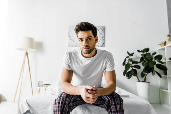 Bel homme sérieux en pyjama assis sur le lit à la maison — Photo de stock