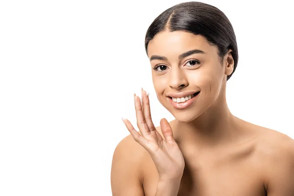 Hermosa chica afroamericana desnuda aplicando crema facial y sonriendo a la cámara aislada en blanco - foto de stock