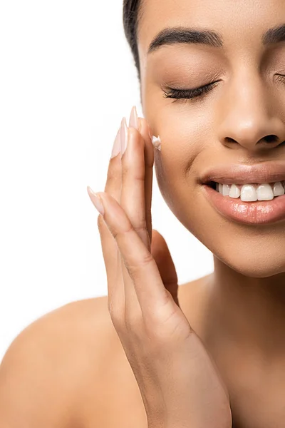 Primer plano vista de feliz joven afroamericana aplicación de crema facial aislado en blanco - foto de stock