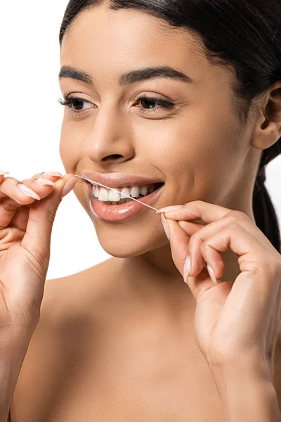 Красивая улыбающаяся молодая африканская американка, пользующаяся зубной нитью и выглядывающая изолированной на белом — стоковое фото