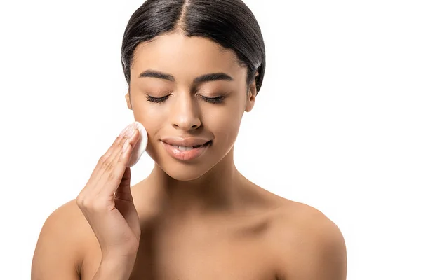 Belle souriante femme afro-américaine nue avec les yeux fermés nettoyage visage avec disque de coton isolé sur blanc — Photo de stock