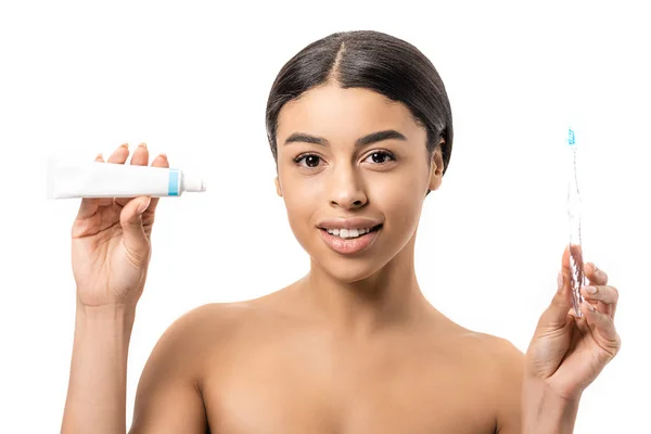 Приваблива афроамериканська жінка тримає зубну щітку з зубною пастою і посміхається на камеру ізольовано на білому — стокове фото