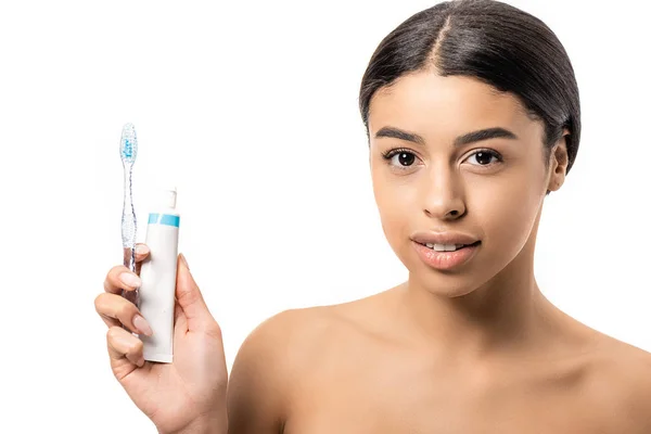 Atractiva joven afroamericana mujer sosteniendo cepillo de dientes con pasta de dientes y mirando a la cámara aislada en blanco - foto de stock