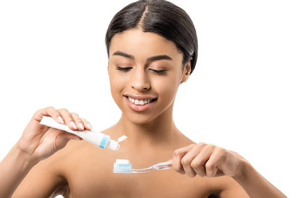 Красива усміхнена гола афроамериканка тримає зубну щітку і зубну пасту ізольовано на білому — стокове фото