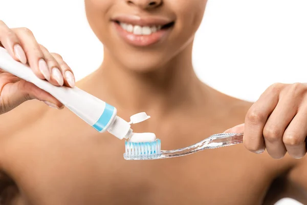 Обрезанный снимок улыбающейся молодой африканской женщины с зубной щеткой и зубной пастой, изолированной на белом — стоковое фото