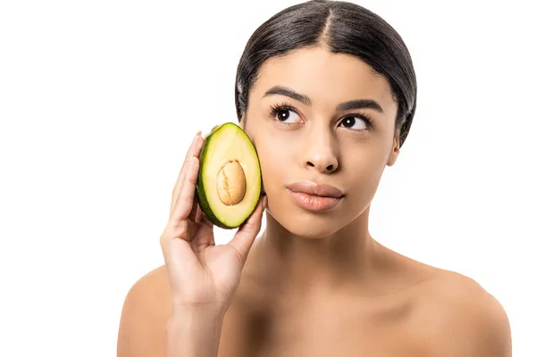 Nachdenkliche junge afrikanisch-amerikanische Frau hält Avocado in der Hand und blickt isoliert auf weiß — Stockfoto