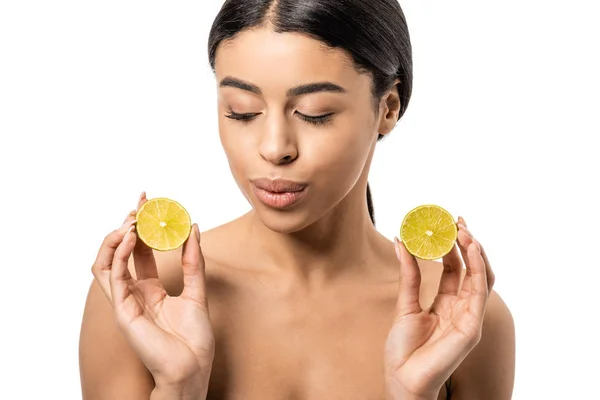 Beautiful naked african american girl holding halves of lime and looking down isolated on white — Stock Photo