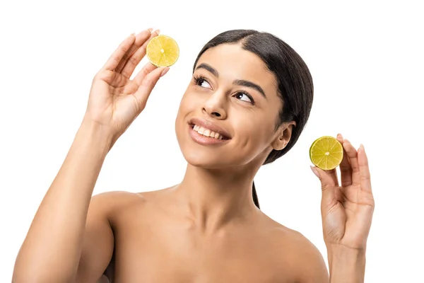 Smiling naked african american girl holding halves of lime and looking up isolated on white — Stock Photo