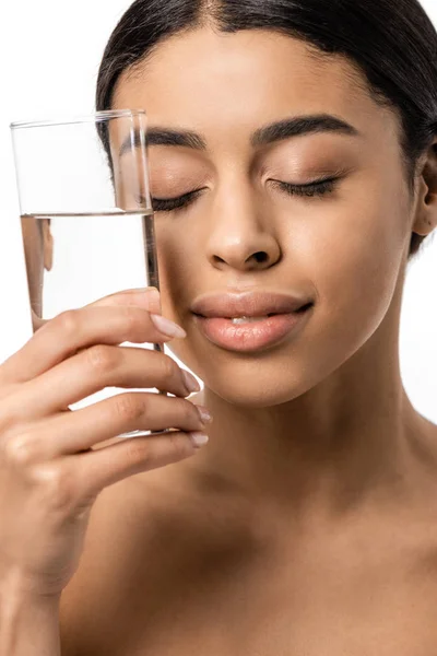 Bela jovem afro-americana com olhos fechados segurando vidro de água clara perto do rosto isolado no branco — Fotografia de Stock