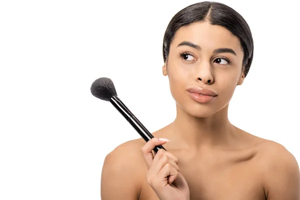 Cher jeune femme africaine américaine nue tenant pinceau de maquillage et regardant loin isolé sur blanc — Photo de stock