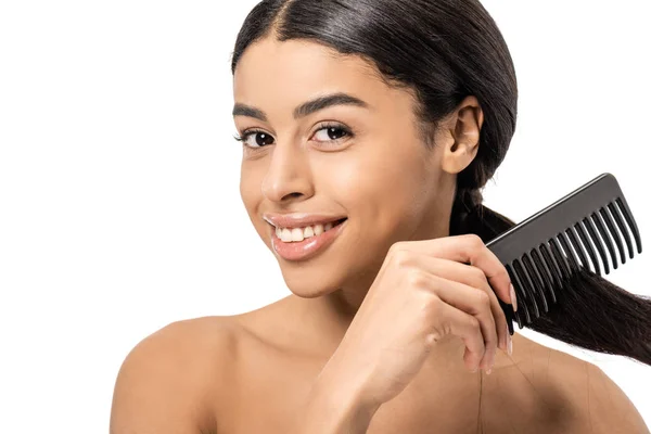 Atractivo desnudo joven afroamericano mujer peinando el pelo y sonriendo a la cámara aislado en blanco - foto de stock