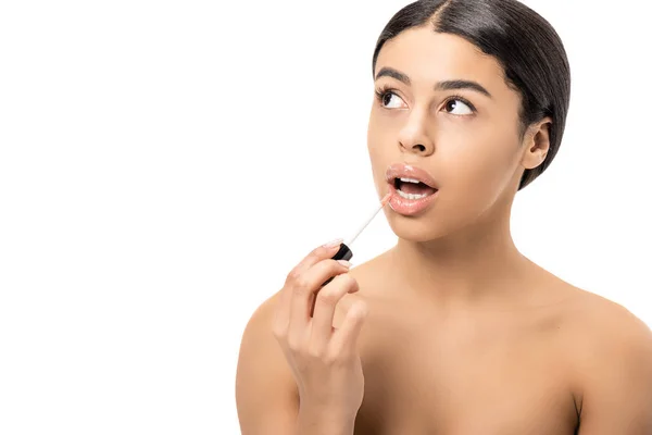Atractiva chica afroamericana desnuda aplicando brillo de labios y mirando hacia arriba aislado en blanco - foto de stock