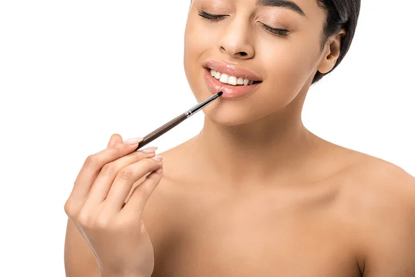 Bela sorridente mulher americana africana nua aplicando batom com escova cosmética isolada no branco — Fotografia de Stock
