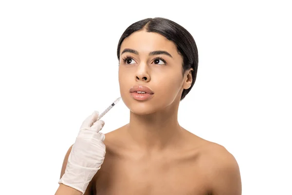 Обрезанный снимок косметолога в латексной перчатке, делающий инъекцию красоты обнаженной молодой африканской женщине, изолированной на белом — стоковое фото