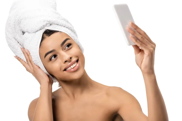 Hermosa joven afroamericana feliz con toalla en la cabeza tomando selfie con teléfono inteligente aislado en blanco - foto de stock