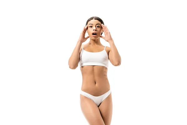 Scioccato afro-americano ragazza in biancheria intima bianca si tiene per mano vicino al viso e guardando la fotocamera isolata su bianco — Foto stock