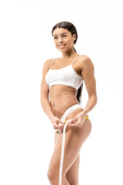 Beautiful smiling young african american woman in underwear measuring hips with tape isolated on white — Stock Photo