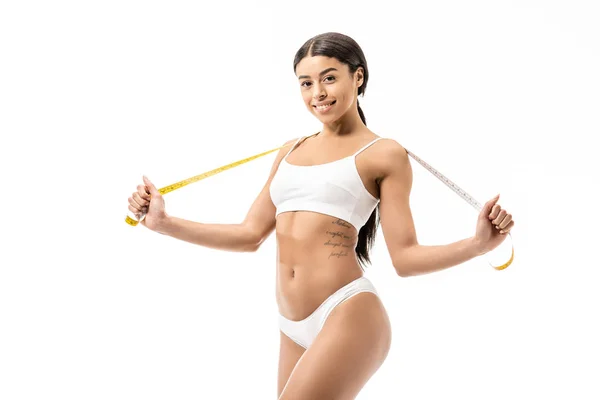 Attractive african american girl in underwear holding measuring tape and smiling at camera isolated on white — Stock Photo