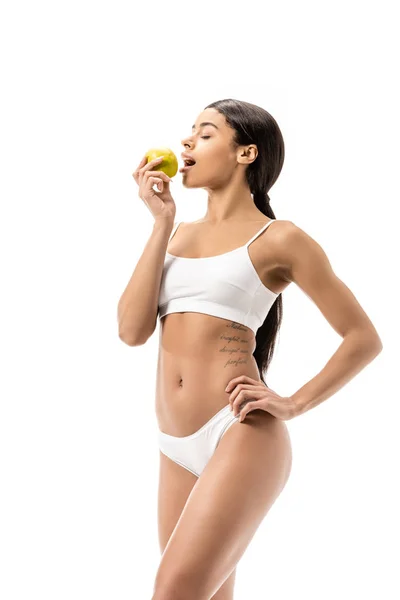 Belle jeune femme afro-américaine en sous-vêtements manger pomme verte isolé sur blanc — Photo de stock