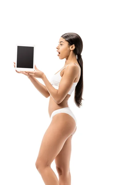Impactado chica afroamericana en ropa interior celebración tableta digital con pantalla en blanco aislado blanco - foto de stock
