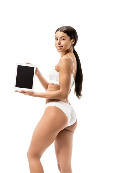 Junge afrikanisch-amerikanische Frau in weißer Unterwäsche mit digitalem Tablet und lächelt isoliert auf weißer Unterwäsche in die Kamera — Stockfoto
