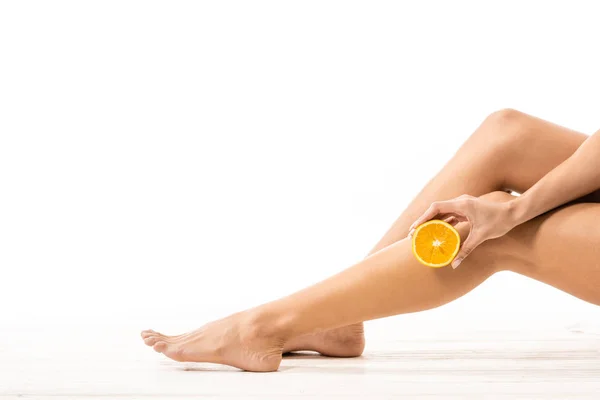 Abgeschnittene Aufnahme schöner weiblicher Beine und der Hälfte Orange in der Hand auf Weiß — Stockfoto