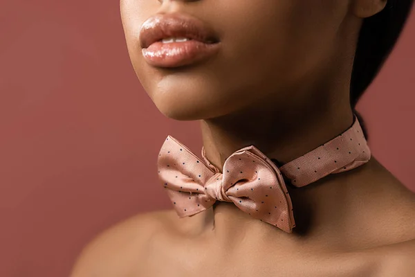 Обрезанный снимок чувственной африканской девушки с розовым галстуком-бабочкой, изолированный на бордовом — стоковое фото