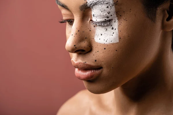 Sensual mulher africana americana com arte corporal criativa no rosto olhando para baixo isolado em marrom — Fotografia de Stock
