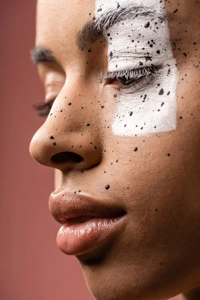 Close-up view of pensive tender african american girl with white paint and brown splashes on face isolated on pink — Stock Photo